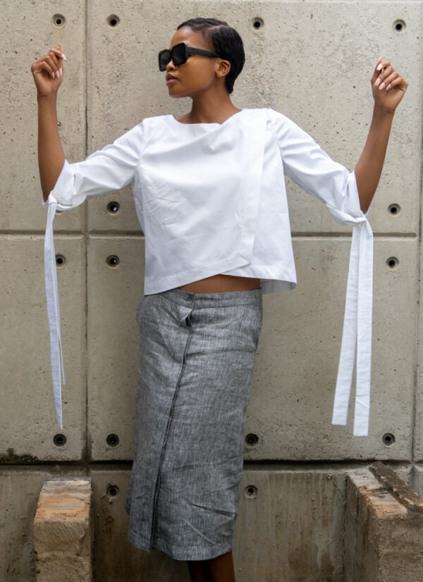 A front view image of a woman wearing an asymmetrical white cotton top with straps